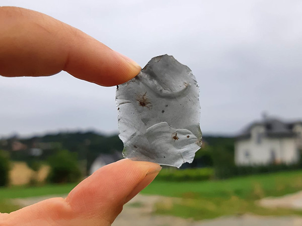 Uniesiony w dwóch palcach pod światło fragment szarego minerału. Jest on tak cienki, że niemal prześwituje