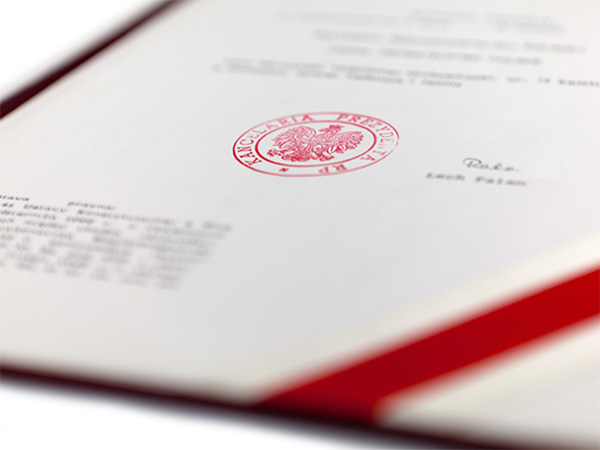 A document with a red seal in an open red cover. The seal shows an eagle with a crown: the emblem of Poland