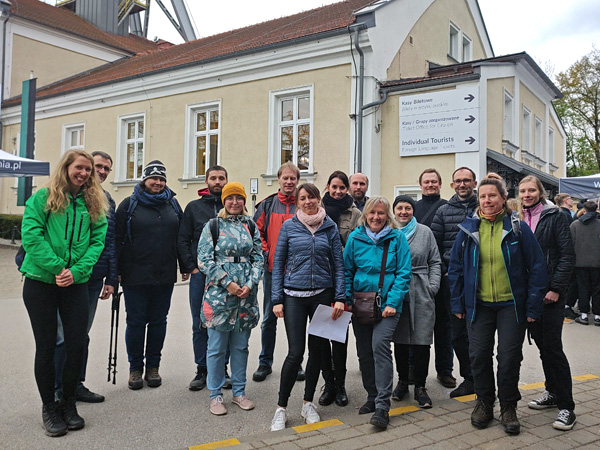 A group of smiling people pose against the background of a historic mine building